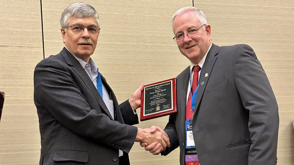 Gary Hein (left) shakes hands with Clark Poppert, 2023 NAICC president, after receiving the Service to Agriculture Award.